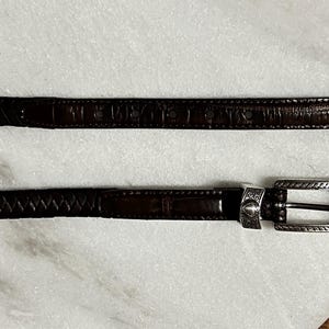 K&ouml;nnte beinhalten: Zwei braune Lederg&uuml;rtel mit silberfarbenen Schnallen. Einer hat eine strukturierte Krokodil-Optik, der andere ein geflochtenes Design. Die Schnallen sind mit dekorativen Details versehen.