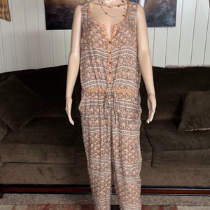 May include: A sleeveless, button-down jumpsuit with a geometric pattern in shades of brown, orange, and white. The jumpsuit has a drawstring waist and wide legs.