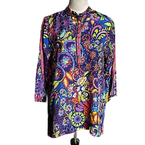 May include: A long-sleeved tunic with a vibrant floral and paisley pattern in shades of blue, purple, pink, yellow, and green. The tunic has a mandarin collar and a button-down placket. The sleeves are three-quarter length.