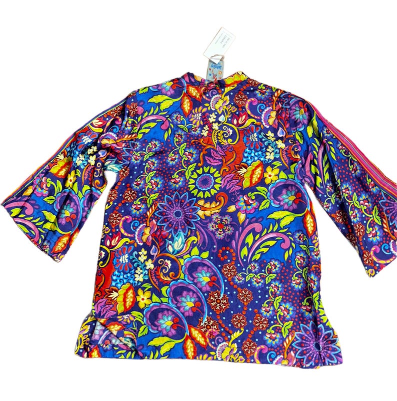 May include: A vibrant, long-sleeved top with a colorful floral and paisley pattern. The top features a blue background with accents of red, yellow, green, and purple. The sleeves are flared, and a tag is attached near the collar.