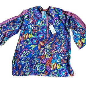 May include: A long-sleeved tunic in a vibrant blue, featuring a colorful floral and paisley pattern. The tunic has a mandarin collar and bell sleeves with striped accents. A tag is attached near the neckline.