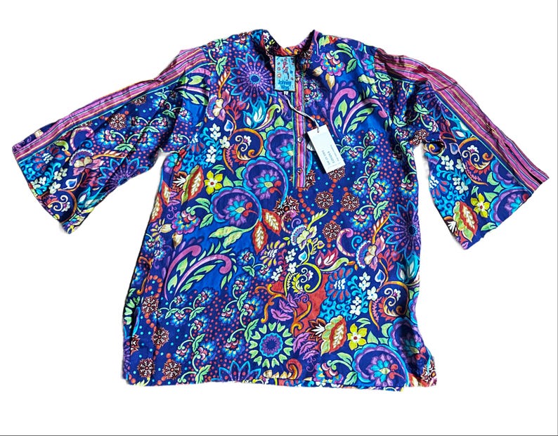 May include: A long-sleeved tunic in a vibrant blue, featuring a colorful floral and paisley pattern. The tunic has a mandarin collar and bell sleeves with striped accents. A tag is attached near the neckline.