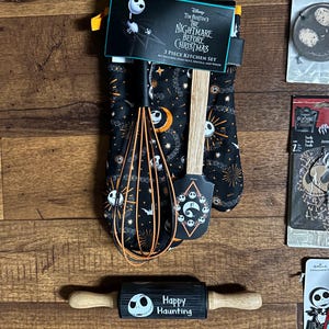 Puede incluir: Un juego de cocina de 3 piezas de Nightmare Before Christmas en negro y naranja. El juego incluye un guante de cocina, una esp&aacute;tula y un batidor. El guante y la esp&aacute;tula presentan dise&ntilde;os de Jack Skellington. Tambi&eacute;n se incluye un rodillo con el texto "Happy Haunting".