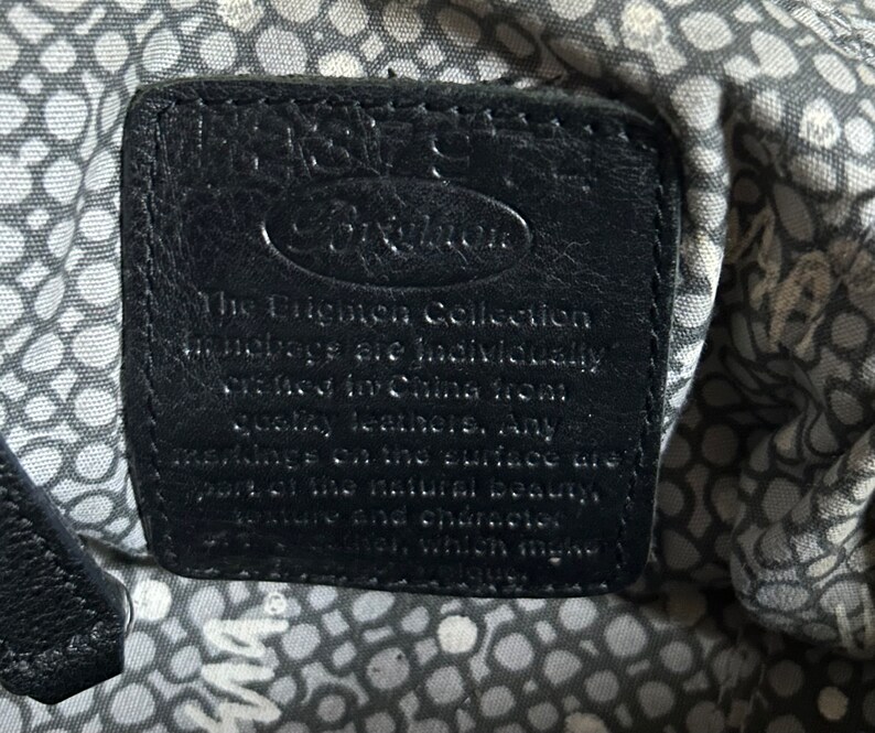 May include: Black leather tag with white text that reads "The Brighton Collection. All leathers are individually selected for China Moon quality leather. Any markings on the surface are part of the natural beauty, texture and character of the leather, which makes each piece unique."
