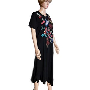 Puede incluir: Un vestido midi negro de manga corta con un dise&ntilde;o bordado colorido en la parte superior delantera. El bordado incluye fresas rojas, p&aacute;jaros azules y varios patrones florales en tonos amarillo, rojo y azul cerceta. Tiene un cuello redondo simple.