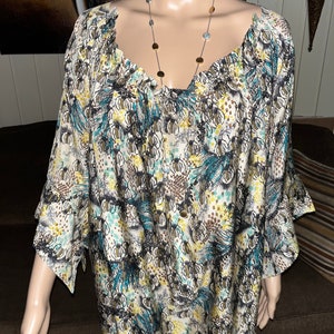 Puede incluir: Una blusa blanca con estampado de color azul y marr&oacute;n, cuello fruncido y mangas 3/4.
