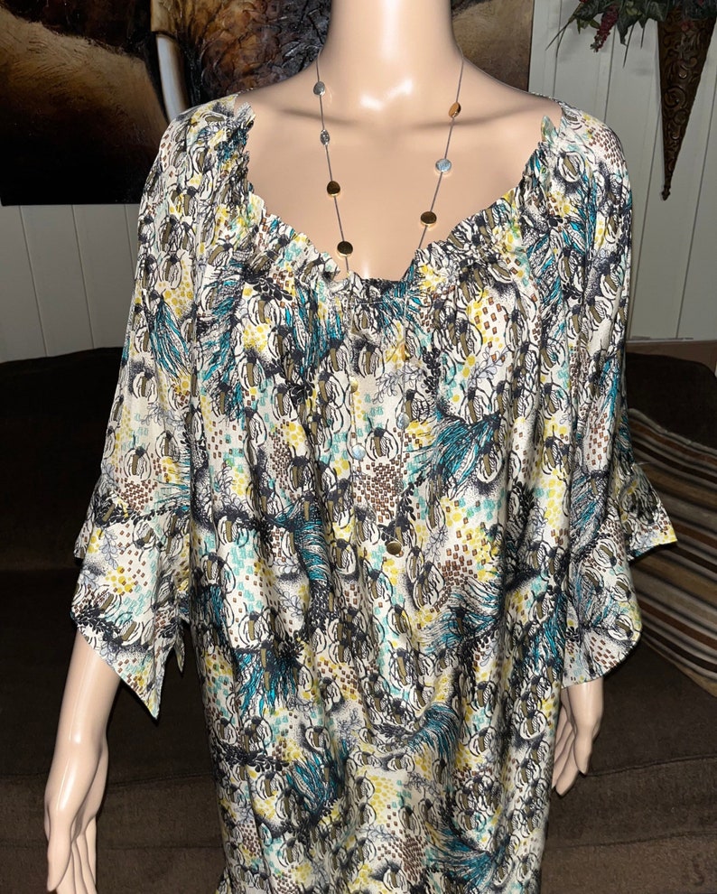Puede incluir: Una blusa blanca con estampado de color azul y marr&oacute;n, cuello fruncido y mangas 3/4.