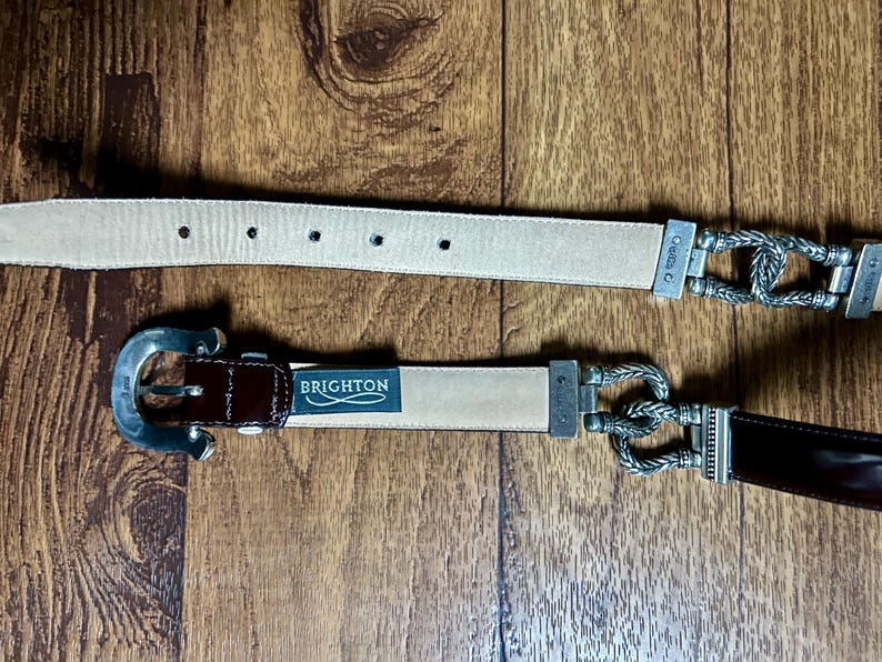Puede incluir: Dos cinturones de cuero con hebillas plateadas. El cintur&oacute;n superior es beige con una hebilla plateada con un dise&ntilde;o de cuerda. El cintur&oacute;n inferior es marr&oacute;n con una hebilla plateada de dise&ntilde;o sencillo. El cintur&oacute;n inferior tiene la palabra "BRIGHTON" impresa.