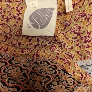 May include: A brown, red, and green patterned fabric with a white tag that says "Lilka" and "Made in China". The tag also has a size "L" on it.