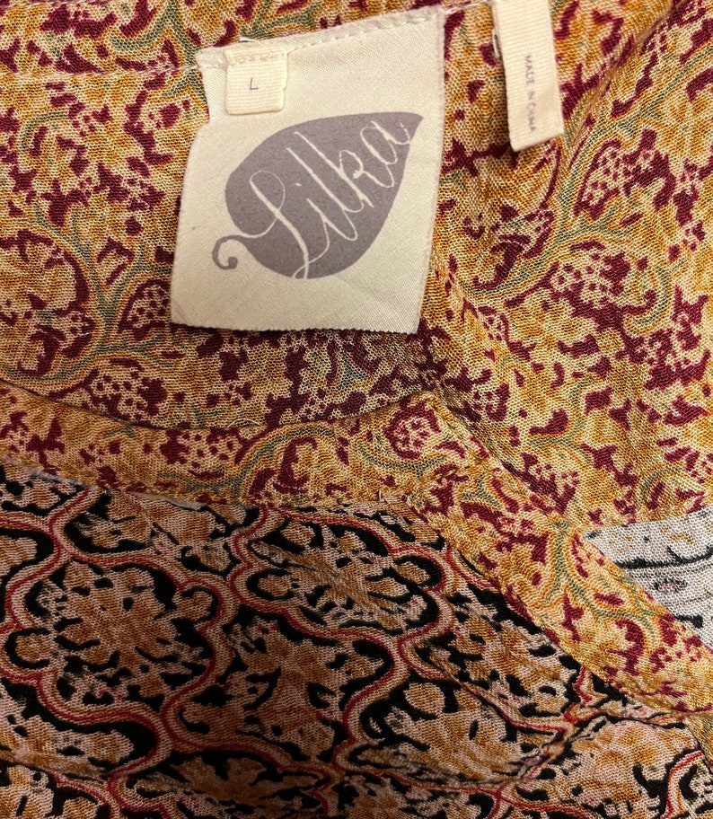 May include: A brown, red, and green patterned fabric with a white tag that says "Lilka" and "Made in China". The tag also has a size "L" on it.