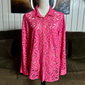 May include: A pink lace button-up shirt with long sleeves. The shirt has a floral pattern and is made of a sheer fabric.