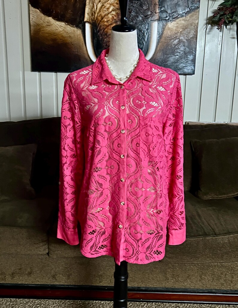 May include: A pink lace button-up shirt with long sleeves. The shirt has a floral pattern and is made of a sheer fabric.