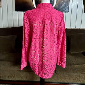 May include: A pink lace blouse with long sleeves and a button-up collar. The blouse has a delicate floral pattern.