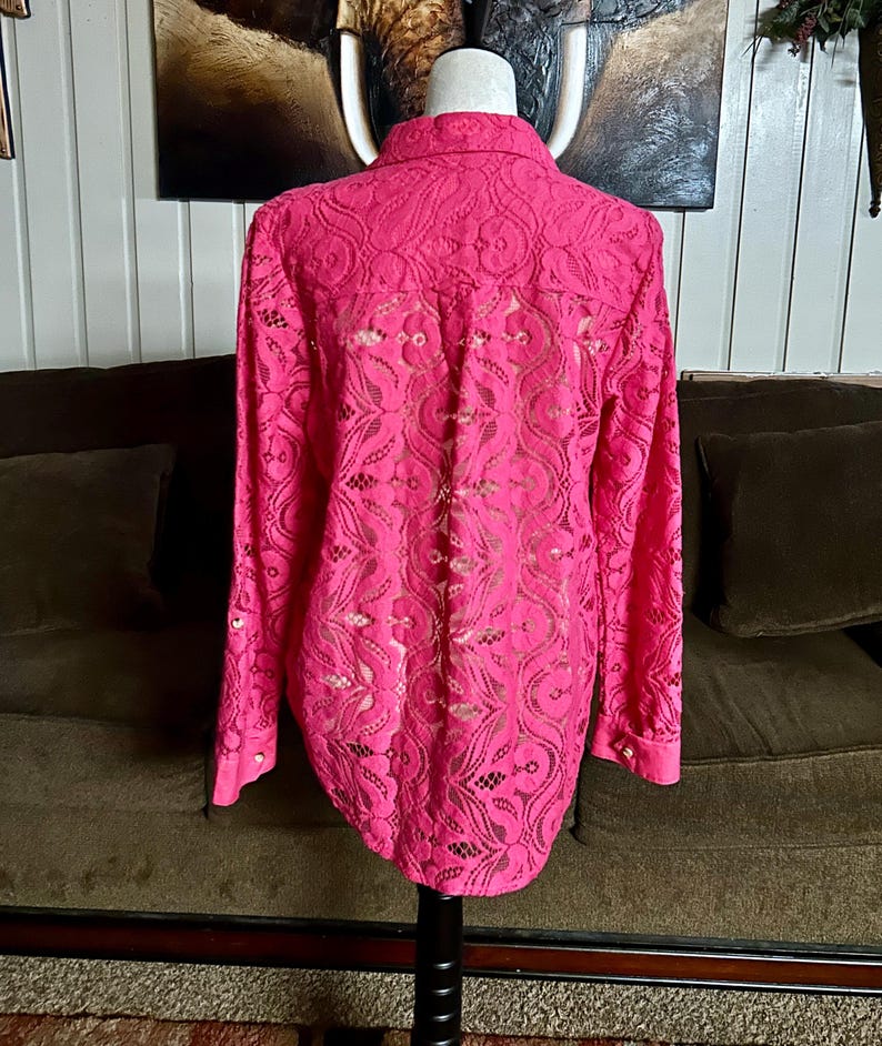 May include: A pink lace blouse with long sleeves and a button-up collar. The blouse has a delicate floral pattern.