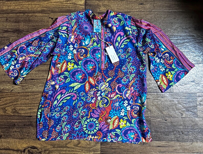 May include: A vibrant, long-sleeved tunic with a colorful floral and paisley pattern in shades of blue, purple, pink, and green. The tunic has a mandarin collar and a zipper closure. The sleeves have a contrasting striped design.