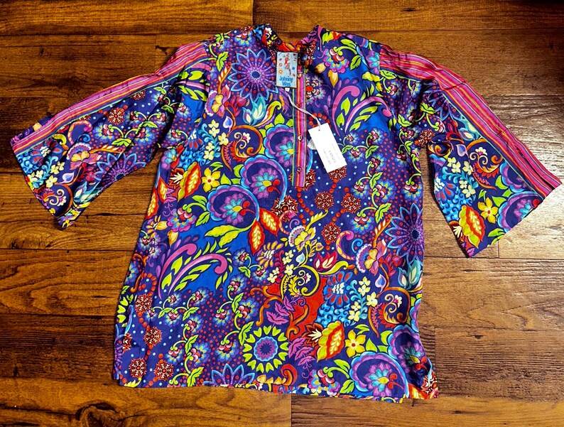 May include: A vibrant, patterned tunic in shades of blue, purple, pink, and yellow. The tunic features a floral design with bell sleeves and a mandarin collar. A tag is attached to the tunic.