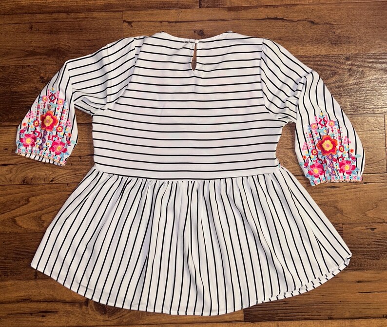 May include: White and black striped blouse with a ruffled hem and floral embroidery on the sleeves.