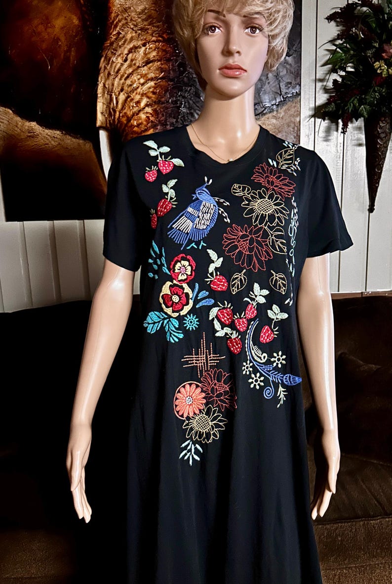 Puede incluir: Una camiseta negra de manga corta con coloridos bordados de un p&aacute;jaro azul, fresas rojas y varias flores en tonos rojos, naranjas, amarillos y azules. El bordado cubre la parte delantera de la prenda con un patr&oacute;n disperso.