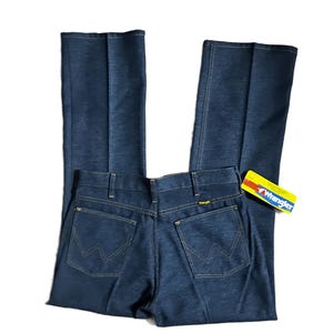 Może przedstawiać: Ciemnoniebieskie dżinsy Wrangler o klasycznym kroju. Dżinsy mają logo Wrangler na tylnej kieszeni oraz ż&oacute;łto-czerwoną metkę. Dżinsy mają prostą nogawkę i klasyczny pięciokieszeniowy design.