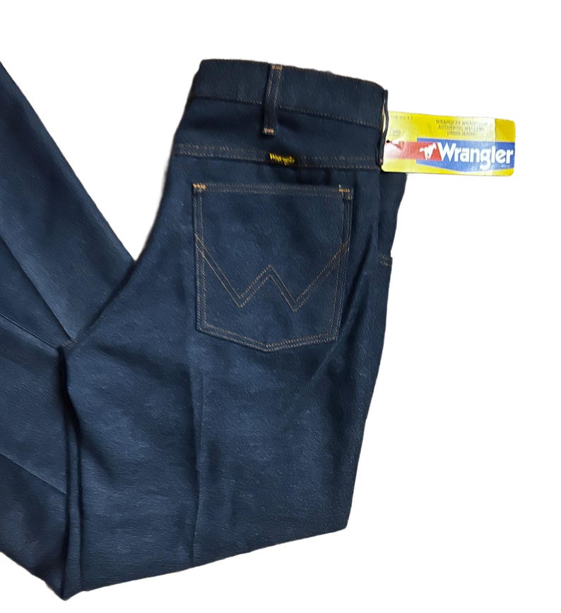 Może przedstawiać: Ciemnoniebieskie dżinsy Wrangler z klasycznym pięciokieszeniowym designem. Tylna kieszeń ma charakterystyczne przeszycia "W" w kontrastującym beżowym odcieniu. Do dżins&oacute;w dołączona jest ż&oacute;łto-czerwona metka Wrangler.