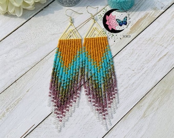 May include: A pair of long, beaded earrings with a geometric design. The earrings are made with a variety of colors, including gold, orange, turquoise, green, and purple. The earrings are hanging from gold hooks.