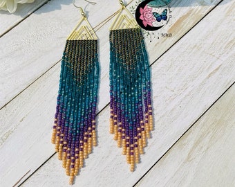 May include: A pair of long, beaded earrings with a gold triangle design. The earrings are made with a gradient of teal, purple, and peach beads.