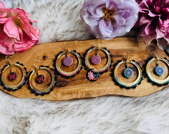 May include: A collection of hoop earrings with various designs. The earrings feature gold-colored hoops adorned with beads and decorative elements. Some earrings have butterfly or floral pendants, while others have colorful beadwork. The earrings are displayed on a wooden surface.