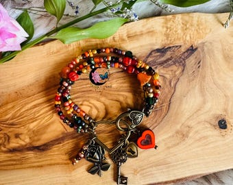 May include: A multi-strand beaded bracelet with a variety of colorful beads in shades of red, orange, yellow, green, and black. The bracelet features several charms, including a heart, a key, and a rose. The bracelet is displayed on a wooden surface.