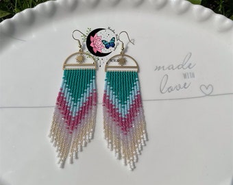 May include: A pair of long, beaded earrings with a gold sun design at the top. The beads are in shades of white, pink, and teal.