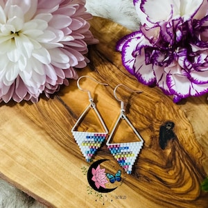 May include: A pair of silver triangle earrings with colourful beaded fringe. The earrings are on a wooden surface with flowers.
