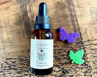 May include: A brown glass bottle with a black dropper and a label that reads "Sedgewitch Essences Firewood Dosage Bottle." The image also includes a purple butterfly, a green leaf, and a small decorative key.
