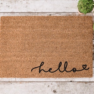 May include: A brown coir doormat with the word "hello" written in black cursive with a small heart at the end.