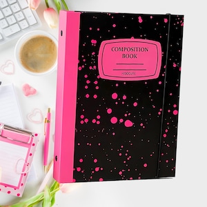 May include: A black composition book with a pink spine and pink splatters. The cover features a pink label with the words "COMPOSITION BOOK" and the brand name "HISOCUTE". A black elastic band secures the book.