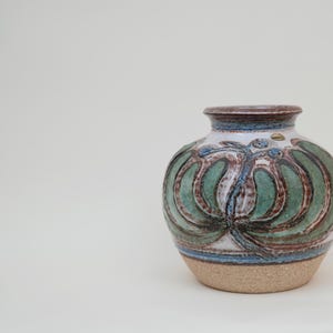Peut inclure: Un vase en céramique blanche avec un motif floral brun, vert et bleu.