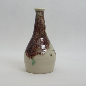May include: A small, white ceramic vase with a brown glaze. The vase has a narrow neck and a rounded body.