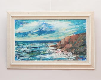 May include: An oil painting in a light-colored wooden frame depicting a coastal scene with a rocky cliffside, turbulent blue and white ocean waves, and a cloudy sky. The artwork features thick, textured brushstrokes in shades of blue, brown, and white.