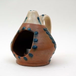 May include: A small, brown ceramic oil lamp with a blue and white glaze. The lamp has a handle and a hole in the side for pouring oil.