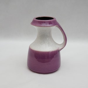 May include: A purple and white ceramic vase with a handle. The vase has a speckled white glaze and a smooth purple glaze.