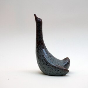 Puede incluir: Escultura de cerámica de un cisne en tonos grises y marrones. El cisne tiene un cuello largo y curvado y un cuerpo redondeado. La escultura es texturizada y tiene un aspecto moteado. Es un artículo decorativo.