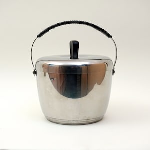 May include: A silver ice bucket with a black handle and lid. The bucket has a rounded shape and a smooth, shiny surface.