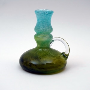 May include: A green and blue glass candle holder with a handle. The holder has a swirl design and a rounded base.