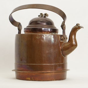 Puede incluir: Una tetera de cobre vintage con asa y tapa de latón. La tetera tiene un acabado deslustrado y una base redonda.