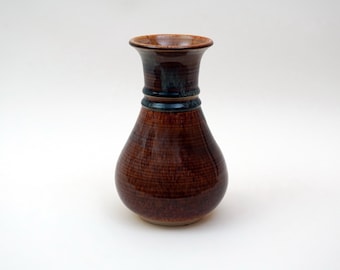 Könnte beinhalten: Eine braune Keramikvase mit einem ausgestellten oberen Rand und einer blauen und braunen Glasur. Die Vase hat eine strukturierte Oberfläche und einen abgerundeten Boden.
