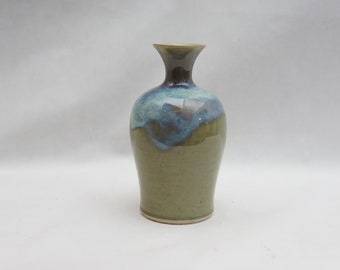 May include: A small, green ceramic vase with a blue and brown glaze. The vase has a narrow neck and a rounded body.