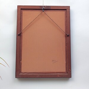 May include: The back of a brown wooden picture frame with a brown paper backing. The frame has a hanging wire attached to it. The year "1965" is written on the backing.