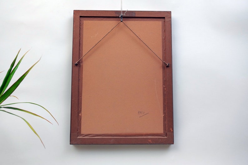 May include: The back of a brown wooden picture frame with a brown paper backing. The frame has a hanging wire attached to it. The year "1965" is written on the backing.