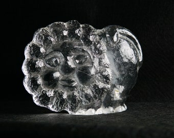 May include: A clear glass sculpture of a face with a detailed, textured design. The face has a large, round head with a wide, open mouth and large eyes. The sculpture is made of clear glass and has a smooth, polished finish.