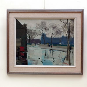 Puede incluir: Una pintura enmarcada que representa una escena callejera con árboles, edificios y personas caminando. La pintura está realizada en un estilo suelto e impresionista, con un enfoque en la luz y el color. La firma del artista es visible en la esquina inferior derecha.