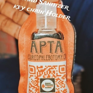 May include: Orange hand sanitizer key chain holder with the text "PERSONALIZED HAND SANITIZER KEY CHAIN HOLDER". The sanitizer bottle has the text "APTA" and a QR code.