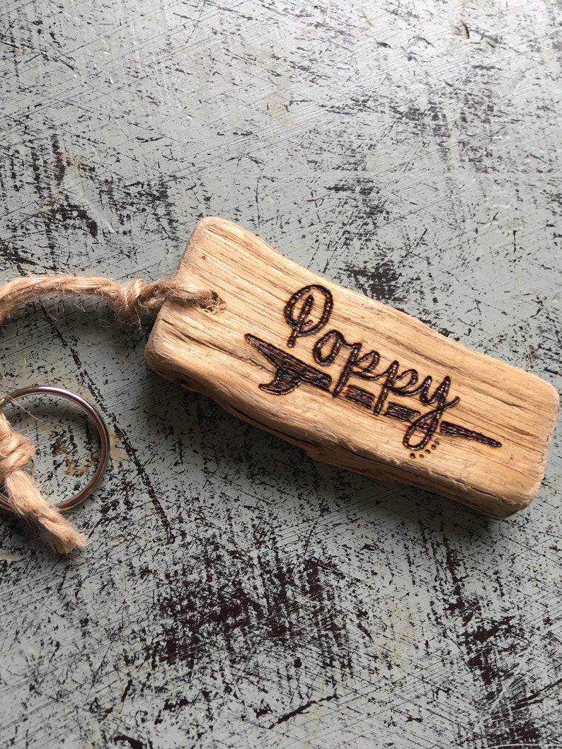 Pu&ograve; includere: Un portachiavi rettangolare in legno galleggiante marrone chiaro con il nome Poppy inciso a fuoco sulla superficie in corsivo. Un anello metallico &egrave; fissato al legno attraverso un piccolo foro utilizzando un pezzo di spago di juta naturale.